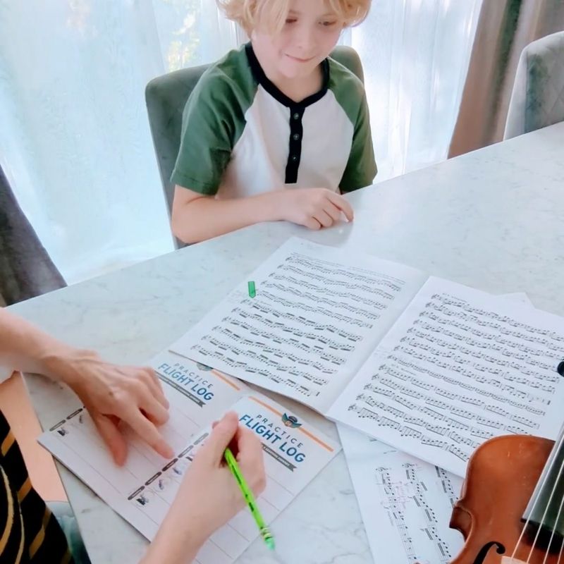 Box filling out a practice passport with his parent next to a music book and a violin.