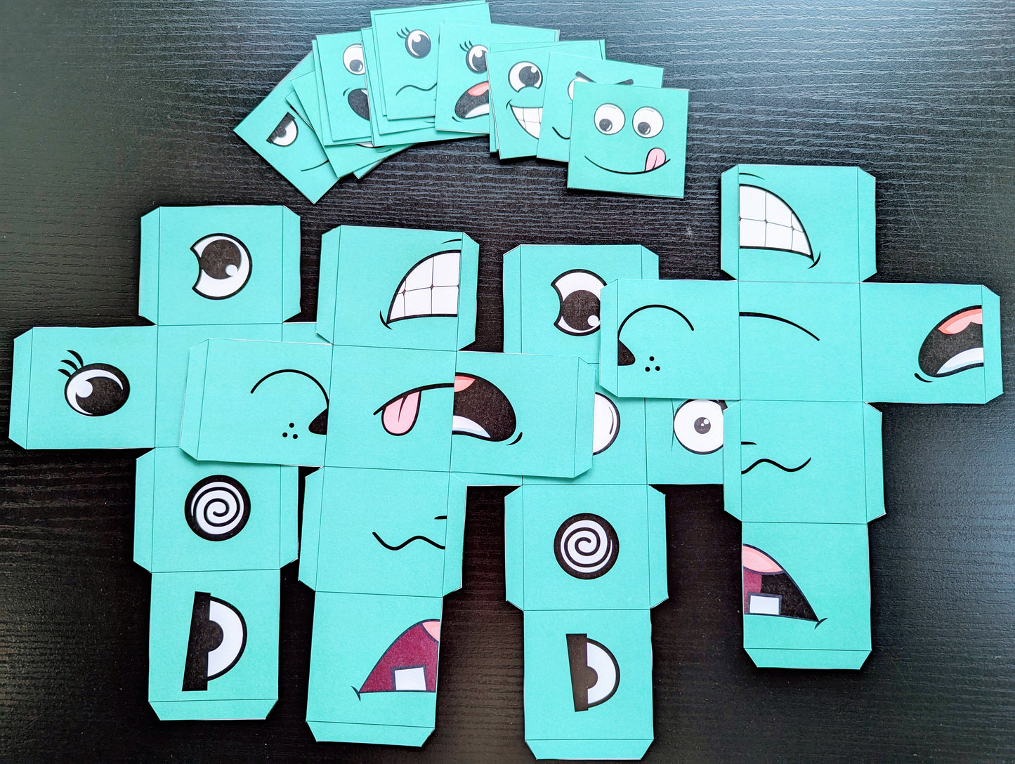 Turquoise cardboard characters with various facial expressions on a dark surface