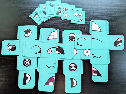 Turquoise cardboard characters with various facial expressions on a dark surface